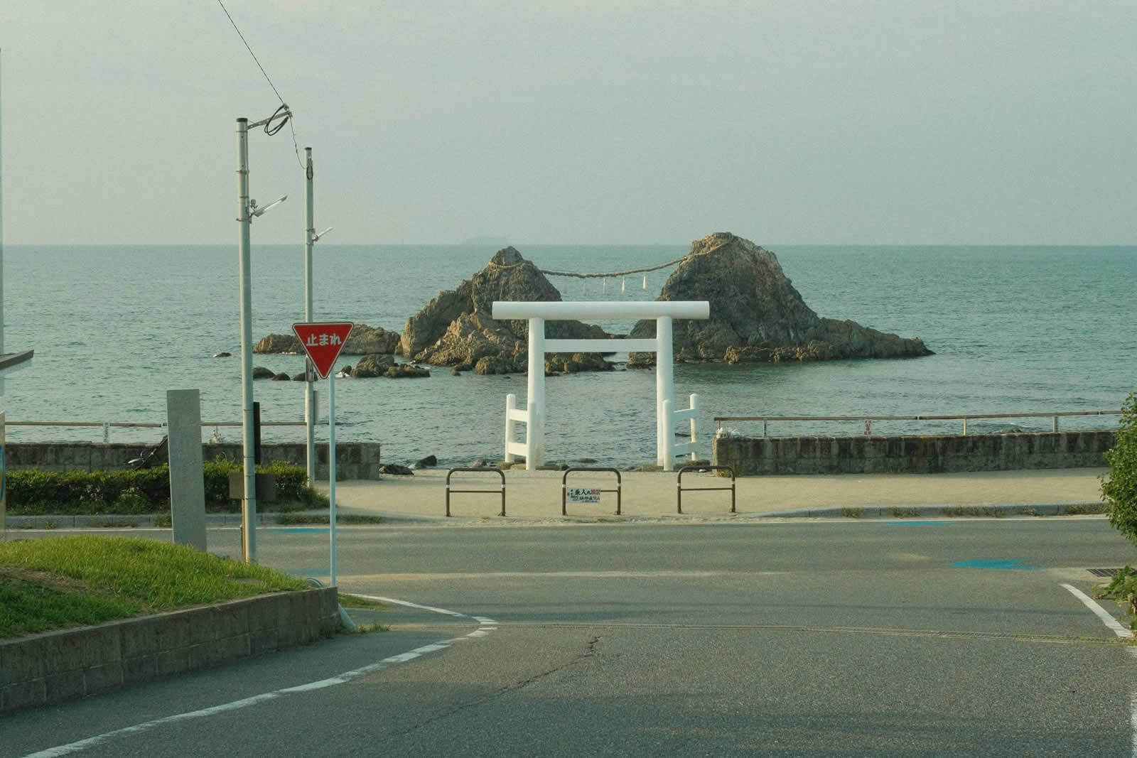 Coastal road ending at Kamakura High School, with a white torii gate and Meoto Iwa (wedded rocks) in view