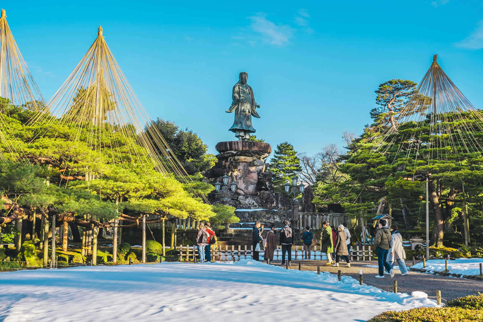 Winter scene in Kanazawa with sunlit snow ropes and statue in garden